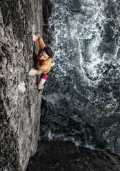 Determined male rock climber climbing cliff by sea - ALRF01815