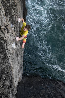 Abenteuerlustiger männlicher Felskletterer klettert auf eine Klippe über dem Meer - ALRF01816