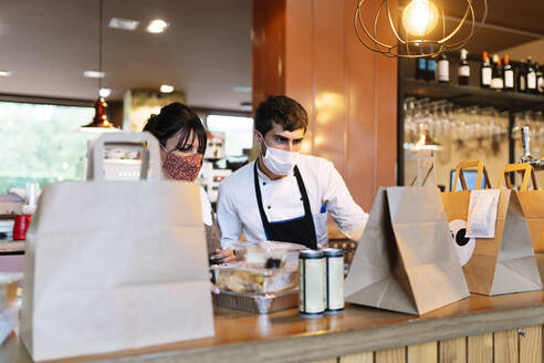 Female owner and male chef checking take out food orders on bar counter during pandemic - DGOF01871