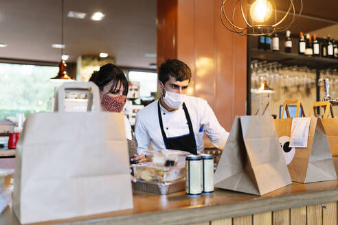Weiblicher Besitzer und männlicher Koch überprüfen die Essensbestellungen an der Theke während der Pandemie - DGOF01871