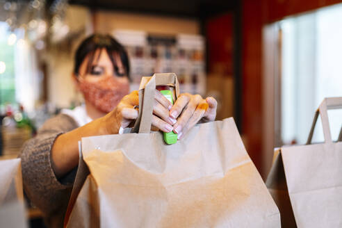 Mature female owner stapling brown paper bag while working in bar during COVID-19 - DGOF01881