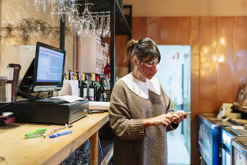 Weibliche Managerin, die in einem Restaurant während der Pandemie ein Smartphone am Computer benutzt - DGOF01886