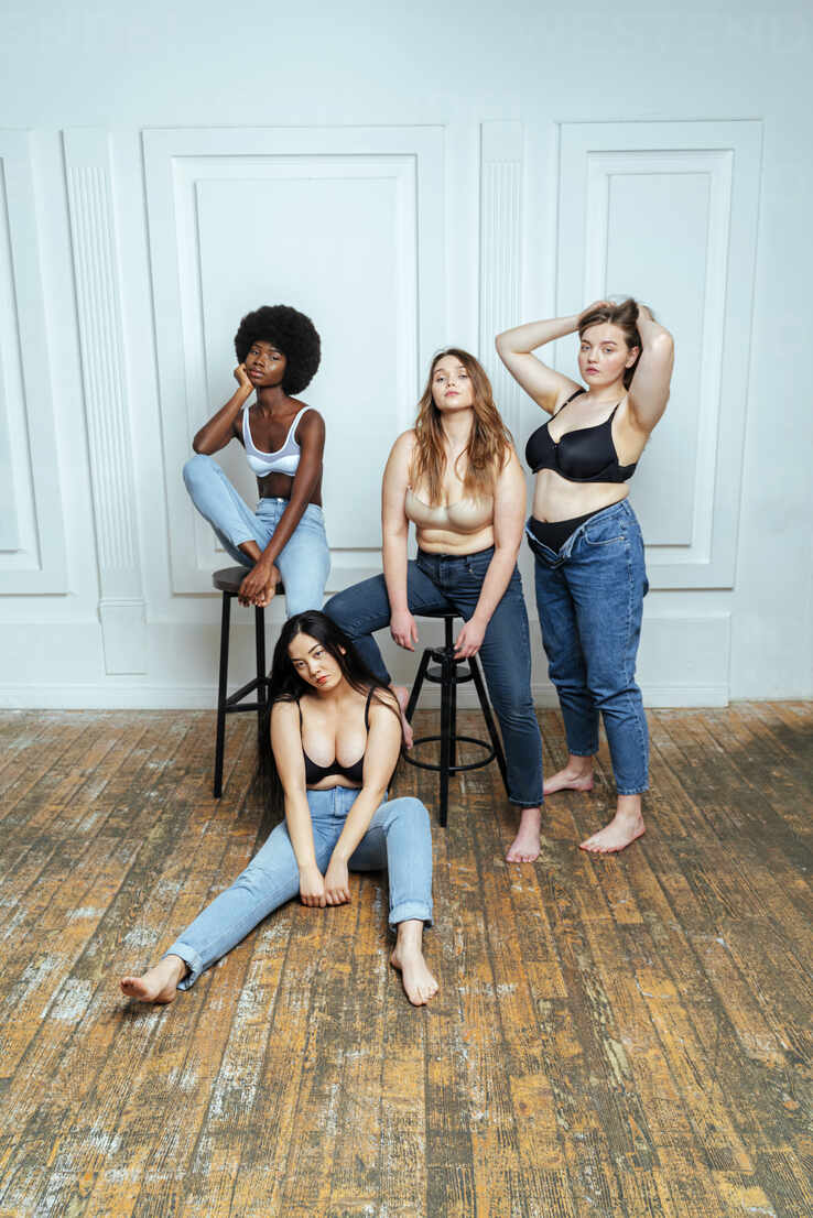 Multi-ethnic group of women wearing bras and jeans posing against wall  stock photo