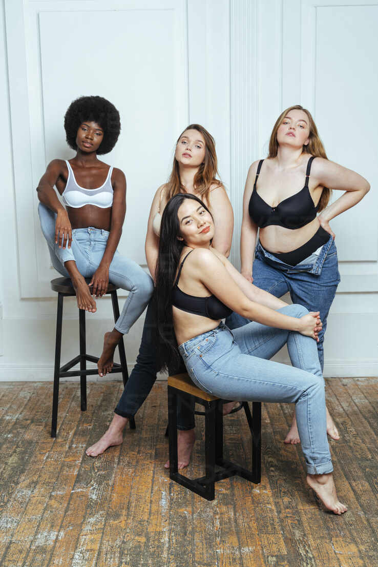 Confident multi-ethnic group of women in bras and jeans posing against wall  stock photo