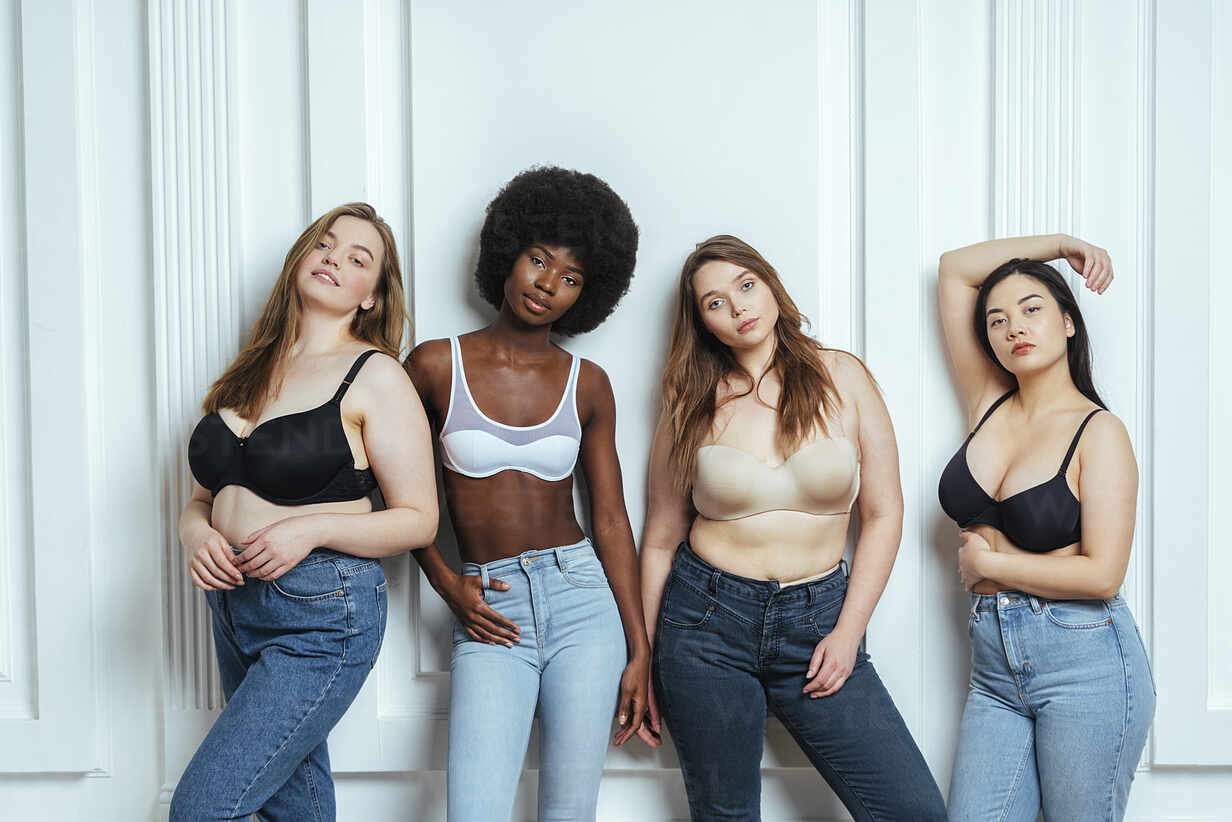 Multi-ethnic group of female models wearing bras and jeans posing against  wall stock photo