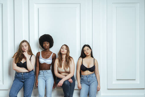 Multi-ethnische Gruppe von Modemodellen, die BHs und Jeans tragen und gegen eine Wand posieren - OIPF00090