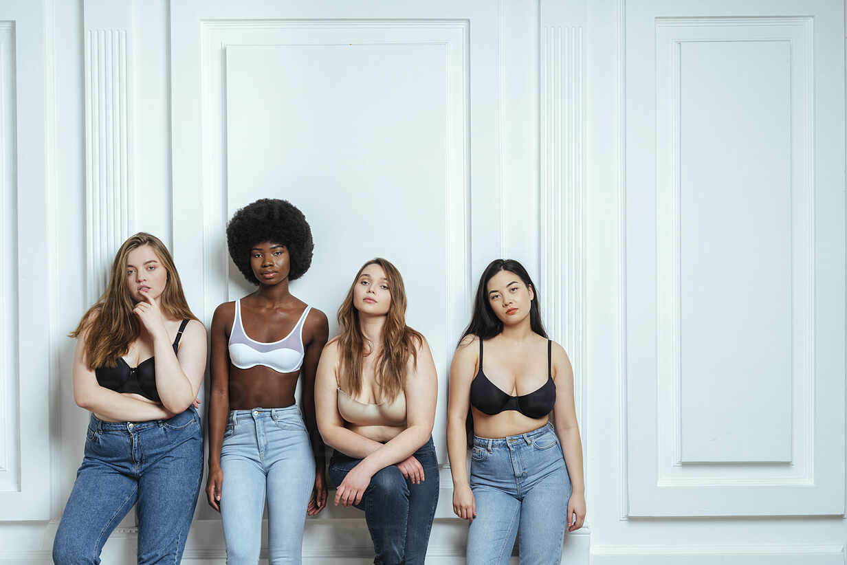 Multi-ethnic group of fashion models wearing bras and jeans posing against  wall stock photo