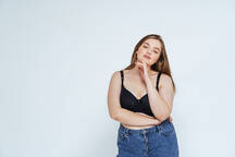 Curvy young woman wearing bra and jeans standing against white