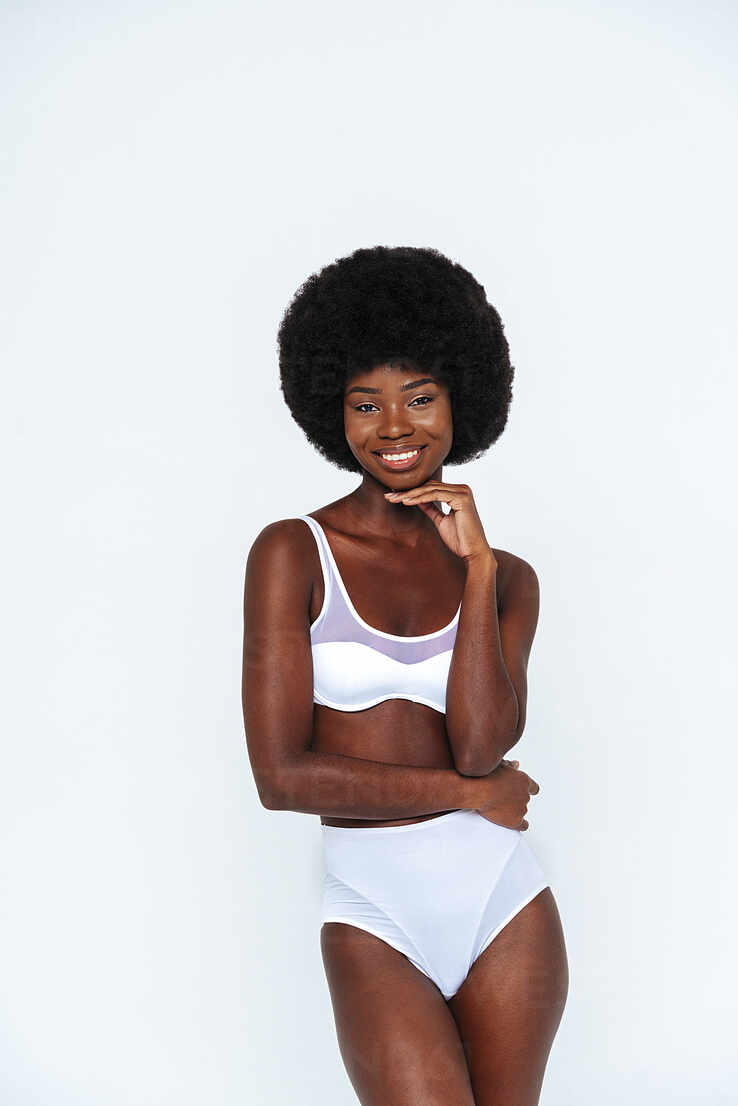 Skinny young woman with afro hair wearing lingerie standing against white  background stock photo