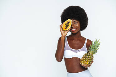 Afro junge Frau in Unterwäsche hält Papaya und Ananas vor weißem Hintergrund - OIPF00113