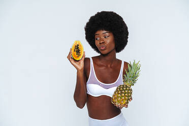 Junge Frau in Unterwäsche hält Papaya und Ananas vor weißem Hintergrund - OIPF00114