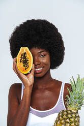 Nahaufnahme einer afroamerikanischen jungen Frau, die eine Ananas und eine Papaya vor weißem Hintergrund hält - OIPF00116