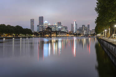 Beleuchtete Wolkenkratzer, die sich in der Themse spiegeln, bei klarem Himmel in der Abenddämmerung, Canary Wharf, London, UK - WPEF03954