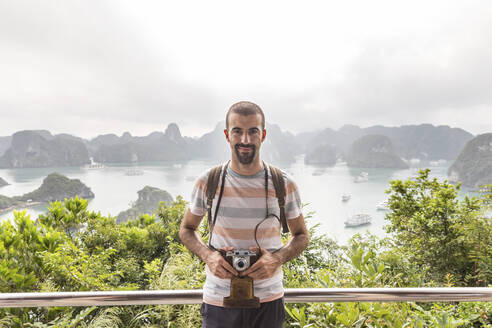 Lächelnder Mann mit Oldtimer-Kamera auf einem Beobachtungspunkt an der Halong-Bucht, Vietnam - WPEF03955