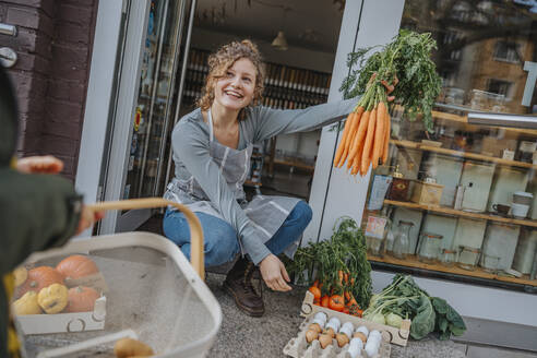 Eine Verkäuferin zeigt einer Kundin im Bioladen Karotten - MFF06871