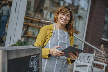 Lächelnde Unternehmerin, die ein digitales Tablet hält, während sie vor einem Einzelhandelsgeschäft steht - MFF06892