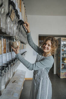 Lächelnde Verkäuferin bei der Arbeit in einem Zero-Waste-Laden mit Lebensmittelspender - MFF06907
