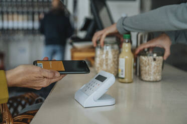 Mature customer with mobile phone paying through bar code scanner in retail store - MFF06927