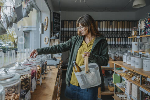 Woman wearing eyeglasses with basket shopping in zero waste shop - MFF06943