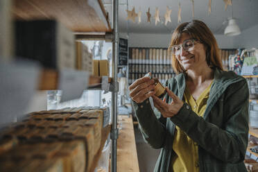 Smiling mature woman looking at label on bottle while shopping in retail shop - MFF06944