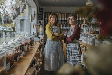 Smiling female coworkers with arms crossed standing in retail shop - MFF06952