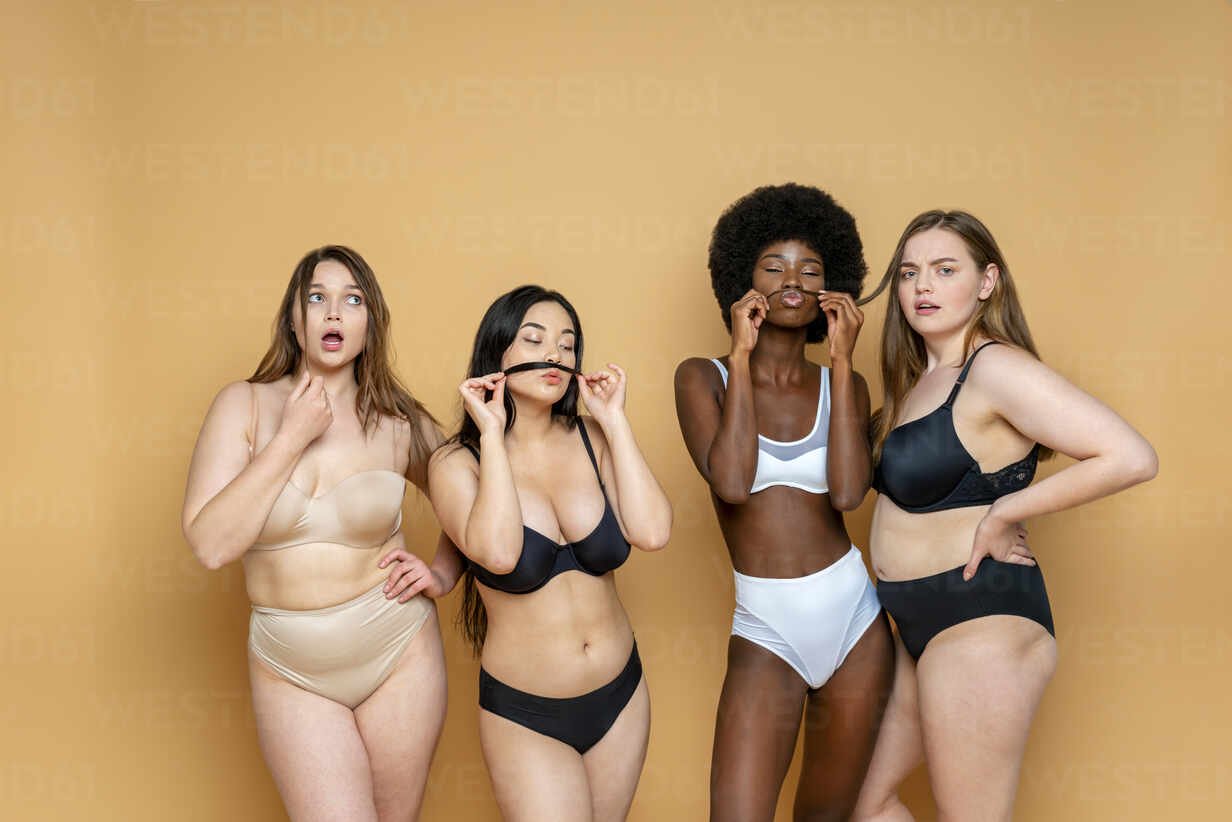Multi-ethnic group of female models in lingerie standing against yellow  background stock photo