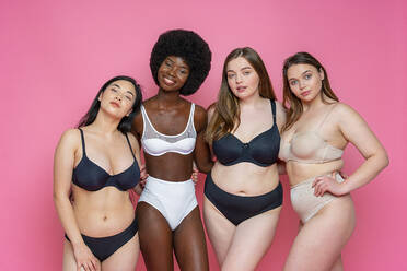 Multi-ethnische Gruppe von weiblichen Modellen in Dessous, die mit den Armen um die Taille vor einem rosa Hintergrund stehen - OIPF00144