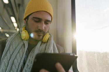 Man using digital tablet while sitting by window in train - EGAF01540