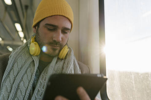 Mann benutzt digitales Tablet, während er im Zug am Fenster sitzt - EGAF01540