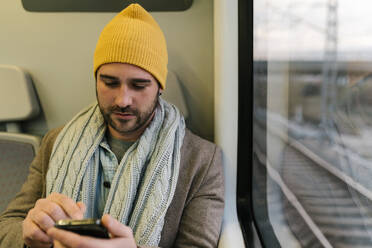 Mann benutzt Mobiltelefon, während er im Zug sitzt - EGAF01561