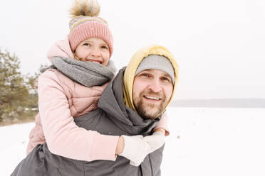 Smiling father piggybacking daughter on snowy land against clear sky - EYAF01490