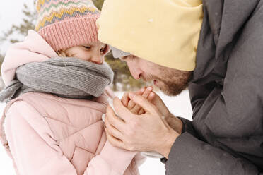 Nahaufnahme eines Vaters, der die kalten Hände seiner Tochter im Winter wärmt - EYAF01491