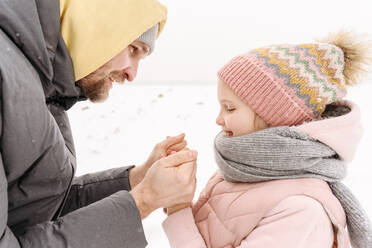 Nahaufnahme eines Vaters, der im Winter die kalten Hände seiner Tochter hält - EYAF01493