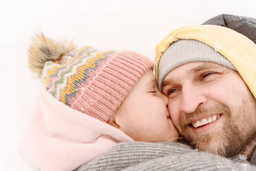 Nahaufnahme einer Tochter, die ihren Vater küsst, während sie im Schnee liegt - EYAF01496
