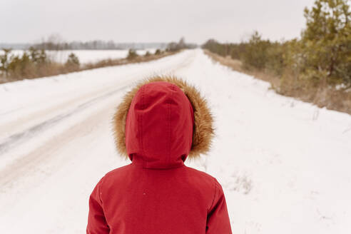 Boy wearing red winter coat standing on snowy landscape - EYAF01505