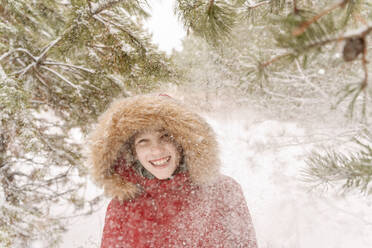 Cheerful boy enjoying snowfall in forest - EYAF01506