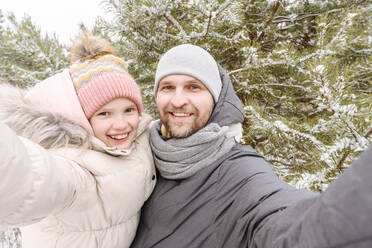 Lächelnder Vater und lächelnde Tochter gegen Bäume im Wald im Winter - EYAF01507