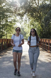 Lächelnde Freundinnen mit Sonnenbrille auf einer Brücke im Wald - JRVF00172