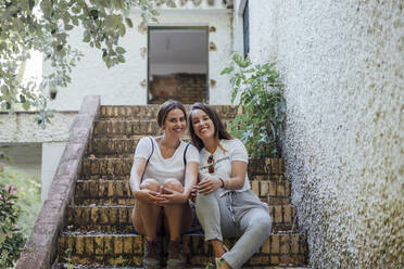 Smiling female friends sitting on steps of old building - JRVF00174