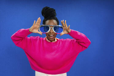 Young female entrepreneur with mouth open wearing novelty glasses against blue wall in office - VPIF03449