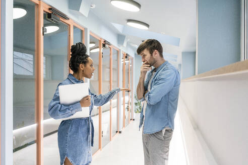 Young businesswoman with laptop arguing with male colleague in corridor at workplace - VPIF03486