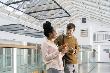 Creative business people discussing while leaning on railing in office corridor - VPIF03499