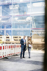 Bauunternehmer, der eine Baustelle mit einer Geschäftsfrau begutachtet, während er am Gebäude steht - PESF02544