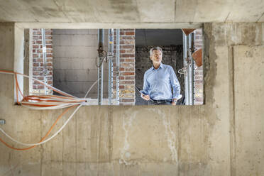Thoughtful architect with digital tablet while standing at construction site - PESF02573