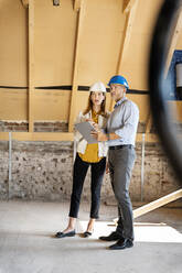 Male architect with digital tablet explaining to businesswoman while standing at construction site - PESF02596