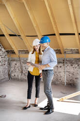 Colleagues wearing hardhat using digital tablet while standing at construction site - PESF02598