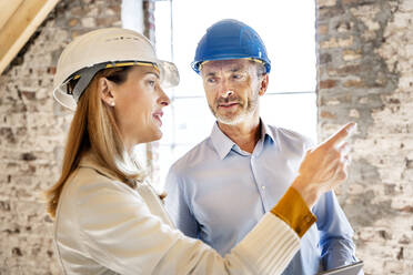 Businesswoman wearing hardhat giving instruction to building contractor while working at construction site - PESF02602