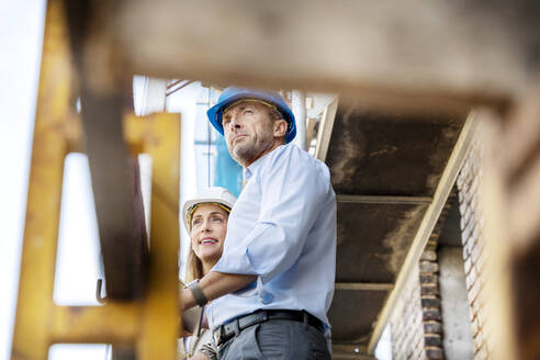Architect looking away while standing by colleague at construction site - PESF02621