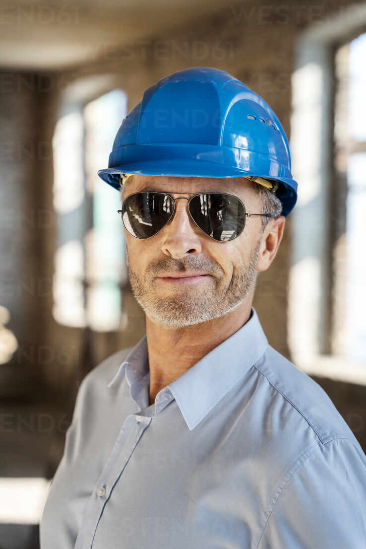 Architect wearing sunglasses and hardhat smiling while standing at  construction site stock photo