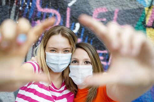Junge Freundinnen, die während der Pandemie gemeinsam ein Fingerbild an einer Graffitiwand anfertigen - IFRF00337